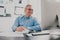 Handsome gray-haired smiling man sits in his office while working on business project , checking his laptop while taking