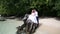 handsome groom embraces brunette bride sitting on rock