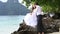 handsome groom embraces brunette bride sitting on rock