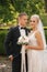 Handsome groom hug his beautiful bride. Newlyweds walking in the park. Blond hair woman in elegant wedding dress