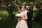 Handsome groom hug his beautiful bride. Newlyweds walking in the park. Brown hair woman in elegant wedding dress