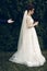 Handsome groom offering his hand to beautiful bride in wedding dress with bouquet, newlywed wife posing in park, proposal concept