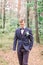Handsome groom in stylish suit standing on the background of pine forest. Beautiful man, groom posing and preparing for
