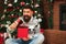 Handsome guy is excited about his Christmas present at home. Happy New Year. Merry Christmas. Bearded man opening red gift box