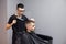 Handsome guy has a haircut in a barbershop, a Kazakh barber dries a client`s hair dryer against a gray wall, a hairdresser makes