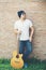 Handsome guy standing holding guitar against the brick wall posing look away. Relaxing holiday.