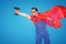 Handsome handyman in red cape and mask as a super hero posing with drill in one hand, isolated on blue studio background . Repair