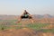 Handsome high jump man. A bald man wearing sunglasses in Hampi, jumps high on Anjaneya Hill, Hanuman Temple. Rice fields or