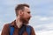 Handsome hipster man with lush beard and mustache on blue sky background. Red bearded guy. Serious brutal male side view