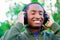 Handsome hispanic black man wearing green sweater in outdoors park area, hands holding headphones covering ears and