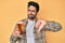 Handsome hispanic man with beard drinking a pint of beer with angry face, negative sign showing dislike with thumbs down,