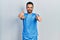 Handsome hispanic man with beard wearing blue male nurse uniform approving doing positive gesture with hand, thumbs up smiling and