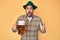 Handsome hispanic man with beard wearing octoberfest hat drinking beer scared and amazed with open mouth for surprise, disbelief