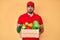 Handsome hispanic man with beard wearing uniform holding delivery food puffing cheeks with funny face