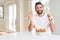 Handsome hispanic man eating chocolate chips muffin surprised with an idea or question pointing finger with happy face, number one