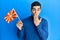 Handsome hispanic man holding macedonian flag covering mouth with hand, shocked and afraid for mistake