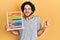 Handsome hispanic man holding traditional abacus screaming proud, celebrating victory and success very excited with raised arm