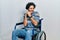 Handsome hispanic man sitting on wheelchair laughing nervous and excited with hands on chin looking to the side