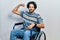 Handsome hispanic man sitting on wheelchair strong person showing arm muscle, confident and proud of power