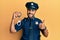 Handsome hispanic man wearing police uniform holding metal handcuffs smiling happy and positive, thumb up doing excellent and