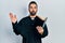 Handsome hispanic priest man with beard holding bible and christian cross making fish face with mouth and squinting eyes, crazy