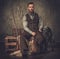 Handsome hunter with a english setter and shotgun in a traditional shooting clothing, sitting on a dark background.