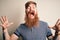 Handsome Irish redhead man with beard and arm tattoo standing over  background celebrating mad and crazy for success with