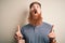 Handsome Irish redhead man with beard and arm tattoo standing over isolated background amazed and surprised looking up and