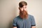 Handsome Irish redhead man with beard and arm tattoo standing over isolated background with serious expression on face