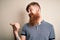 Handsome Irish redhead man with beard and arm tattoo standing over isolated background smiling with happy face looking and