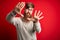 Handsome Irish redhead man with beard wearing casual sweater and glasses over red background doing frame using hands palms and