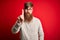 Handsome Irish redhead man with beard wearing casual sweater and glasses over red background Pointing with finger up and angry