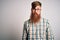 Handsome Irish redhead man with beard wearing glasses and hipster shirt with serious expression on face