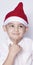 Handsome kid with Santa cap wishing or dreaming something. Child dreaming about Christmas gift. Kid looking up and thinking