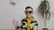 A handsome little boy in sunglasses sits on the floor against the background of a white wall and holds a balloon