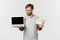 Handsome male freelancer showing laptop screen and money, standing over white background