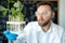 Handsome male microbiologist looking at a green plant in a test tube. Laboratory biologist conducts experiments. Medical