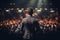 Handsome male motivational speaker holding a microphone in front on an audience. Man in a spotlight talking to a crowd