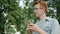 Handsome male student using smartphone in park outdoors smiling enjoying device