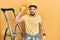 Handsome man with beard by construction stairs wearing hardhat angry and mad raising fist frustrated and furious while shouting