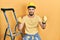 Handsome man with beard by construction stairs wearing hardhat angry and mad raising fists frustrated and furious while shouting