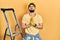 Handsome man with beard by construction stairs wearing hardhat begging and praying with hands together with hope expression on