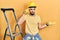 Handsome man with beard by construction stairs wearing hardhat confused and annoyed with open palm showing copy space and pointing