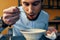 a handsome man with a beard eats borscht in a plate at a table in a cafe and a watch on his hand