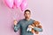 Handsome man with beard expecting a baby girl holding balloons, shoes and teddy bear afraid and shocked with surprise and amazed