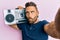 Handsome man with beard holding boombox, listening to music making fish face with mouth and squinting eyes, crazy and comical