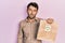 Handsome man with beard holding delivery paper bag with heart reminder looking sleepy and tired, exhausted for fatigue and