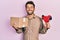 Handsome man with beard holding packing tape holding cardboard smiling with a happy and cool smile on face