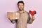 Handsome man with beard holding packing tape holding cardboard smiling looking to the side and staring away thinking