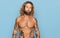 Handsome man with beard and long hair standing shirtless showing tattoos looking at the camera blowing a kiss on air being lovely